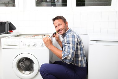 Tesisatçı bozuk çamaşır makinesini tamir ediyor.