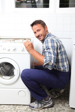 Tesisatçı bozuk çamaşır makinesini tamir ediyor.