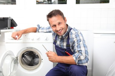 Tesisatçı bozuk çamaşır makinesini tamir ediyor.