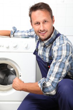 Tesisatçı bozuk çamaşır makinesini tamir ediyor.