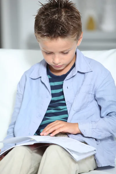 Blong pequeño niño sentado en el sofá con libro — Foto de Stock