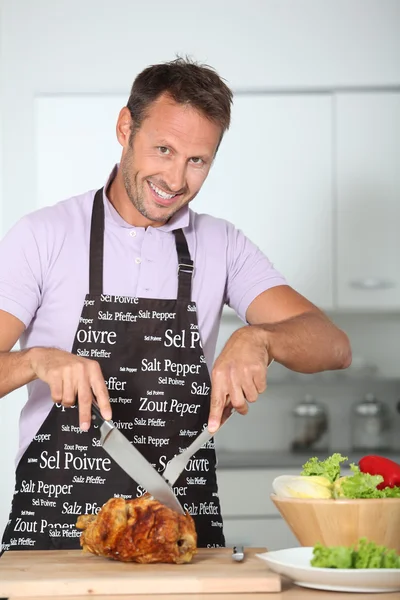 Man in kitchen with apron cooking chicken — Stock Photo, Image