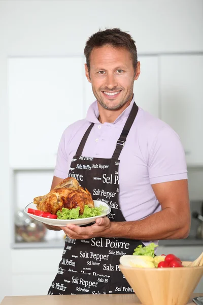 Man in kitchen with apron cooking chicken — Stock Photo, Image