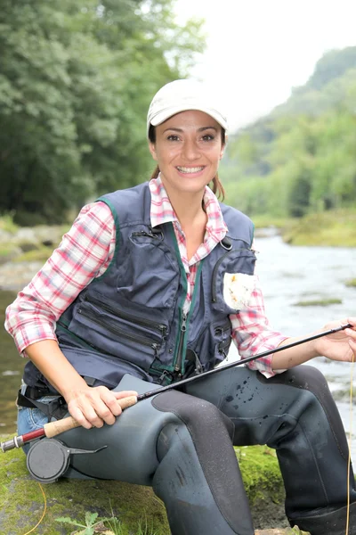 Fisherwoman sitting on stones in river with fishing rod — Stock fotografie