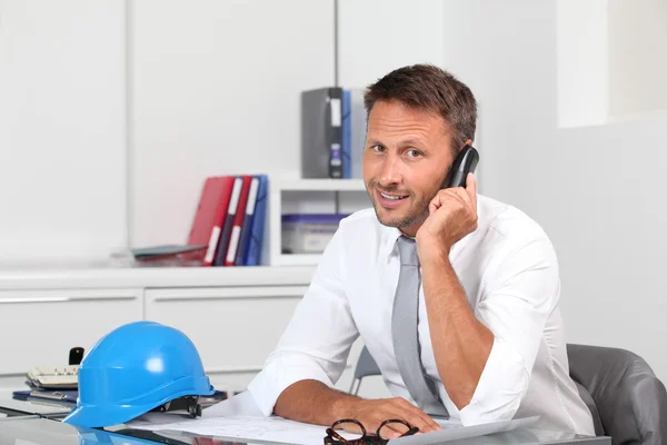 De beheerder van de site in het kantoor met blauwe helm — Stockfoto