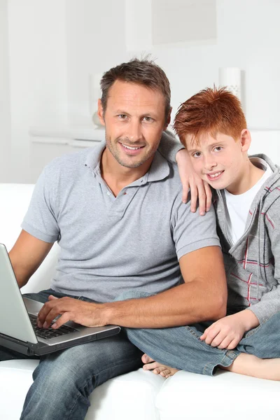 Homem e criança em casa com computador portátil — Fotografia de Stock