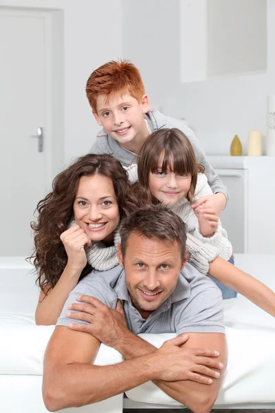 Happy family of 4 laying on a sofa at home — Stock Photo, Image
