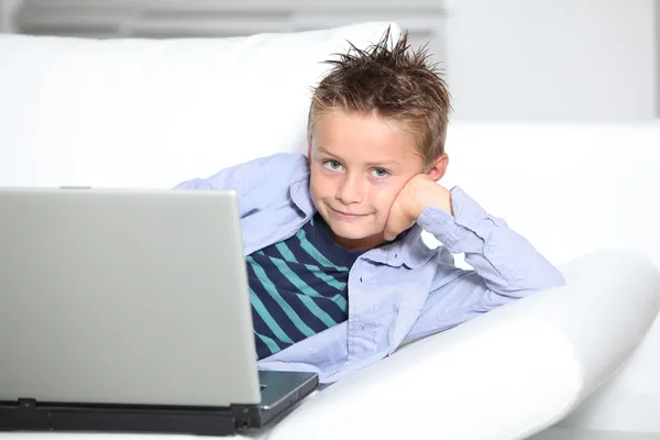 Petit garçon blond assis sur un canapé avec ordinateur portable Photos De Stock Libres De Droits