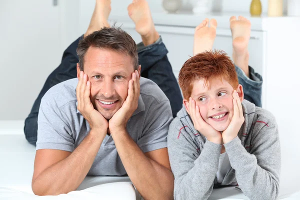 Man with child lying on a sofa at home Stock Picture