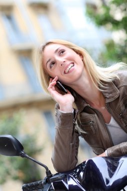 telefon ile motosiklet üzerinde oturan sarışın kız