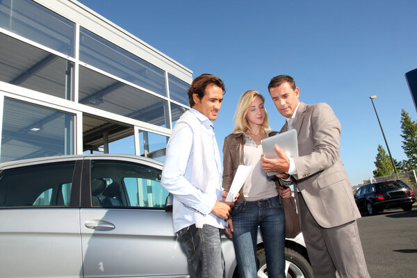 Car seller with couple looking at electronic tablet