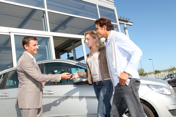 Car seller with couple outside car dealership