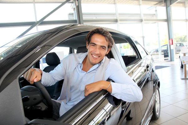 Hombre sonriente sentado al volante de un coche nuevo — Foto de Stock