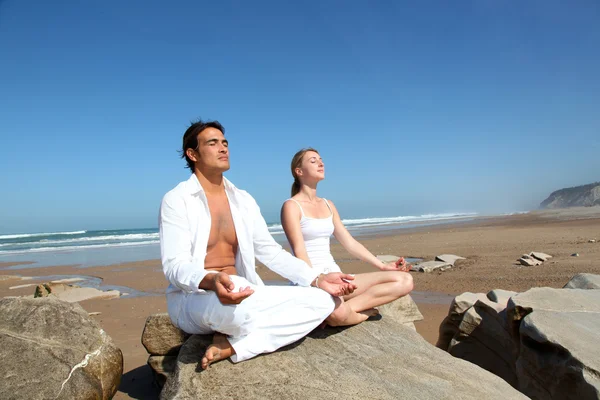 Paar doen yoga oefeningen op het strand — Stockfoto