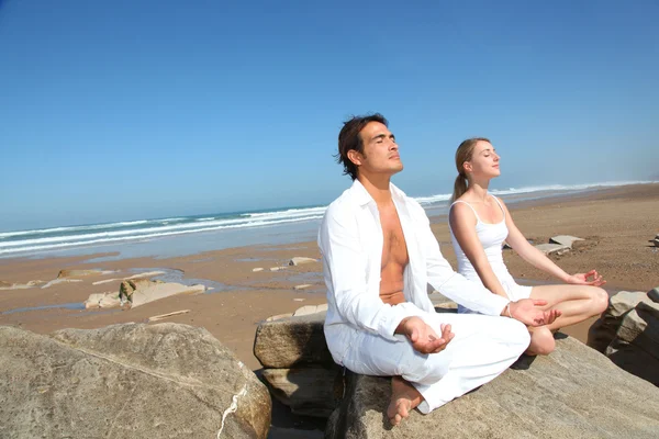 Paar doen yoga oefeningen op het strand — Stockfoto