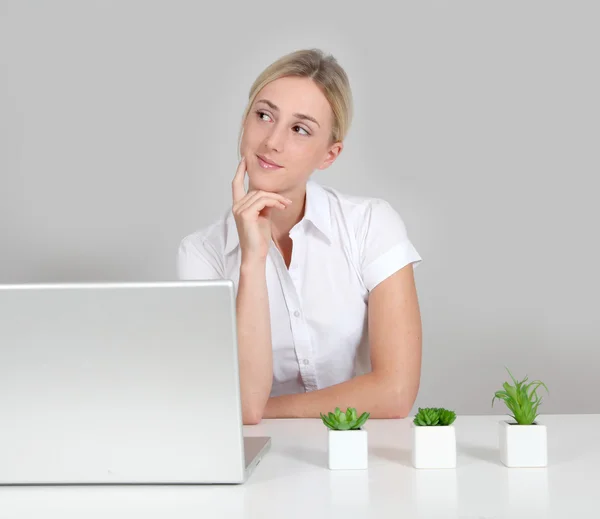 Vaalea nainen istuu tietokoneella ja vihreät kasvit — kuvapankkivalokuva