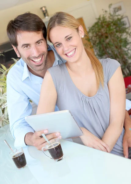 Happy νεαρό ζευγάρι στο σπίτι χρησιμοποιώντας ηλεκτρονικό, ταμπλετών — Φωτογραφία Αρχείου