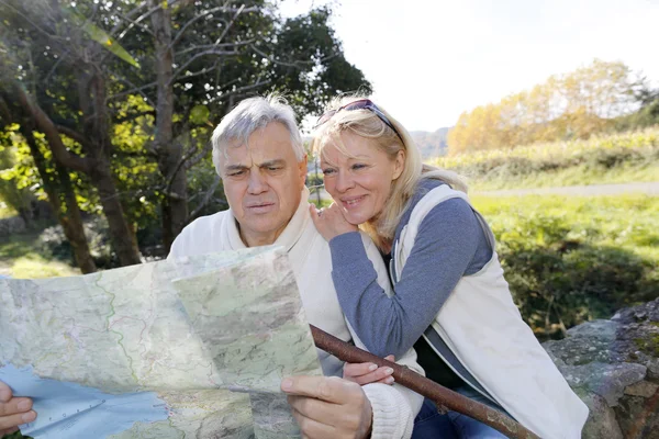 Senior couple sitting by river and looking at map — Stock Photo, Image