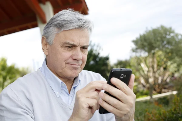 Старший чоловік використовує смартфон в саду — стокове фото