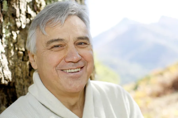 Retrato de un hombre mayor sonriente apoyado en un árbol —  Fotos de Stock