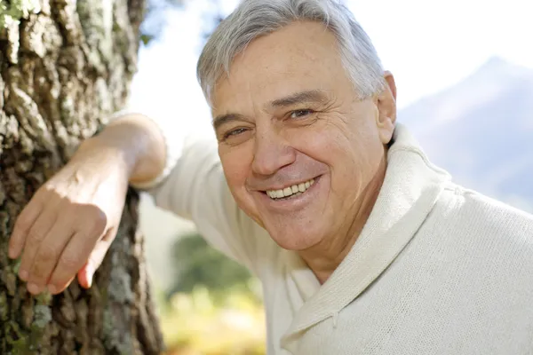 Portret van lachende senior man leunend tegen boom — Stockfoto