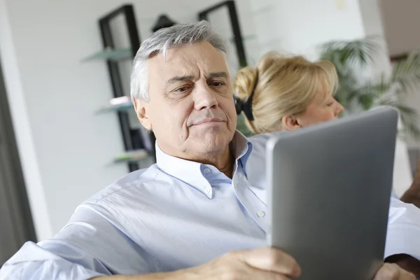 Senior man reading news on tablet sitting in couch — Stock Photo, Image