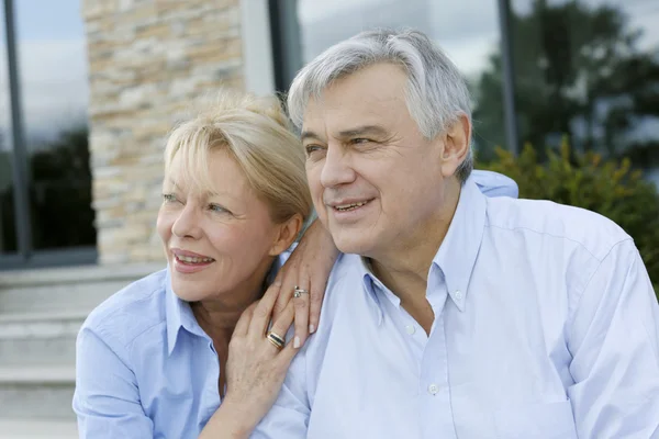 Senior couple sitting in front of house and looking away — Stock Photo, Image