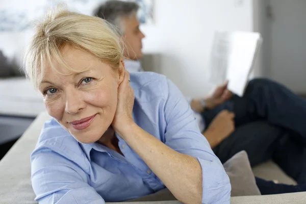 Femme âgée assise sur le canapé, mari en arrière-plan — Photo