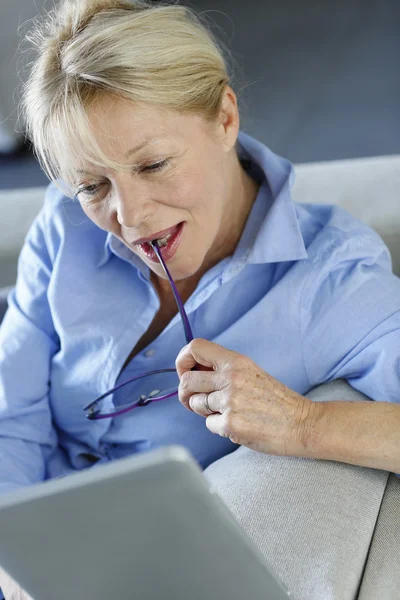 Senior woman using electronic tablet in sofa — Stock Photo, Image