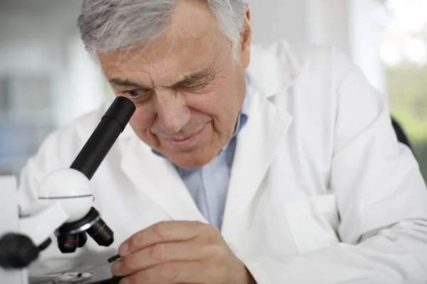 Científico en laboratorio mirando a través de lente de microscopio — Foto de Stock