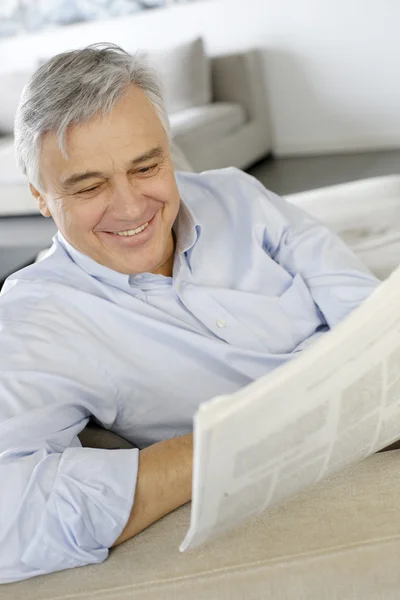 Homem sênior sorrindo como ler o jornal — Fotografia de Stock