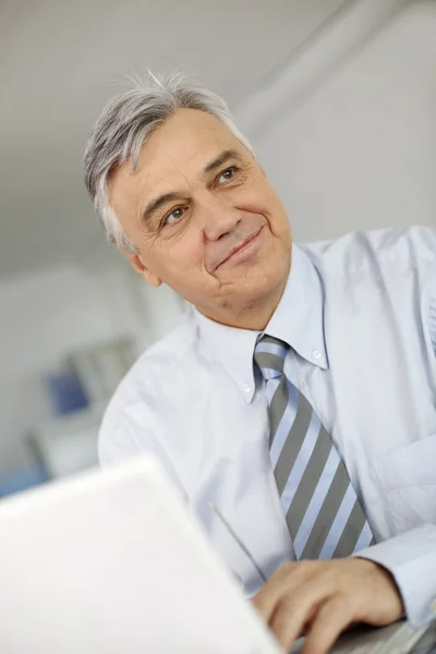 Portret van senior zakenman in office die op laptop werkt — Stockfoto