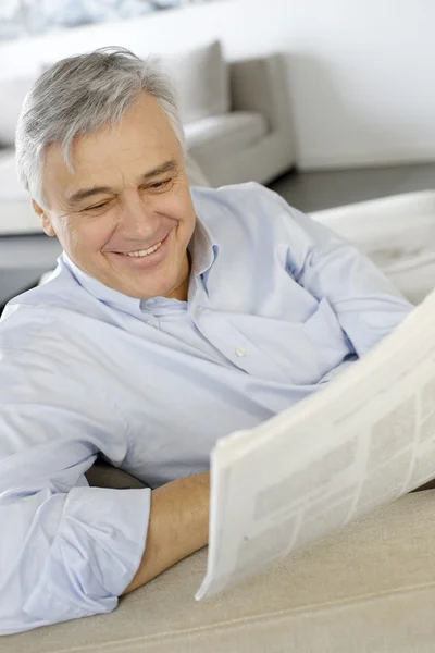 Hombre mayor sonriendo mientras lee el periódico Imagen de stock