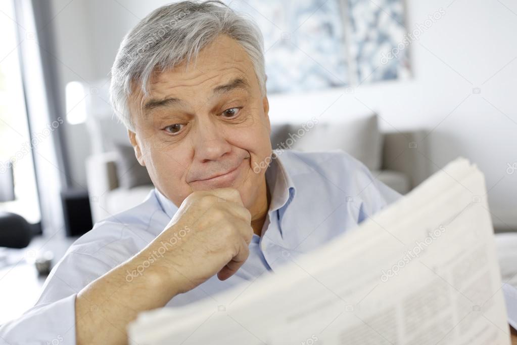 Senior man reading newspaper with puzzled look