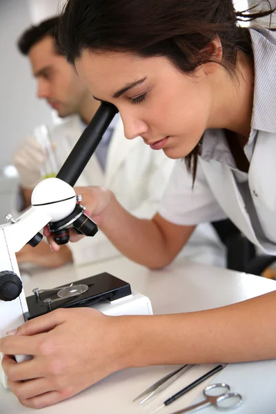 Mujer joven mirando a través del microscopio lente — Foto de Stock