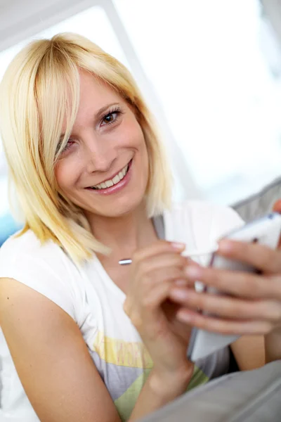 Gülümseyen genç kadın evde smartphone kullanarak — Stok fotoğraf