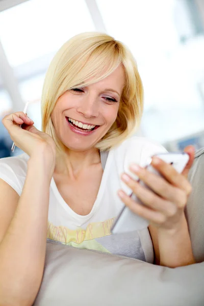 Χαμογελαστά νεαρή γυναίκα στο σπίτι χρησιμοποιώντας smartphone — Φωτογραφία Αρχείου