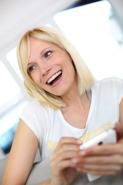 Χαμογελαστά νεαρή γυναίκα στο σπίτι χρησιμοποιώντας smartphone — Φωτογραφία Αρχείου
