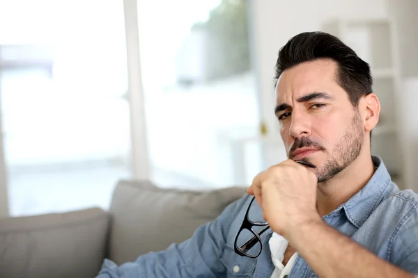 Man sitting in sofa with thoughtful look on his face — Stock Photo, Image