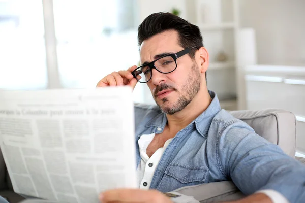 Chico alegre leyendo el periódico en el sofá —  Fotos de Stock