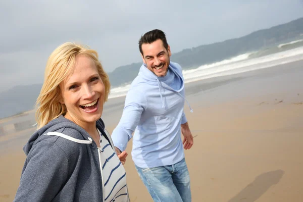 Веселая женщина бегает с мужем по пляжу — стоковое фото