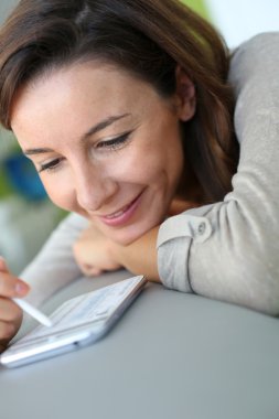 Evde akıllı telefon kullanan genç bir kadın.