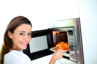 Woman putting plate in microwave oven clipart