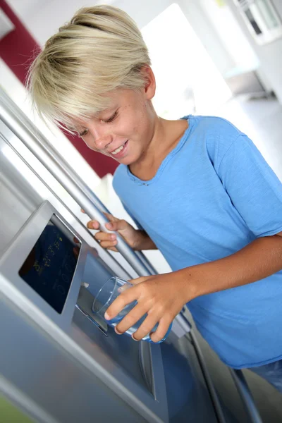 Ung pojke dricksvatten från kylskåp — Stockfoto