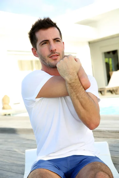 Young man doing stretching exercises on pool deck — Stock Photo, Image