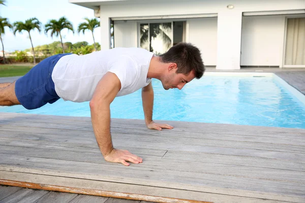 Jovem fazendo flexões no deck da piscina — Fotografia de Stock