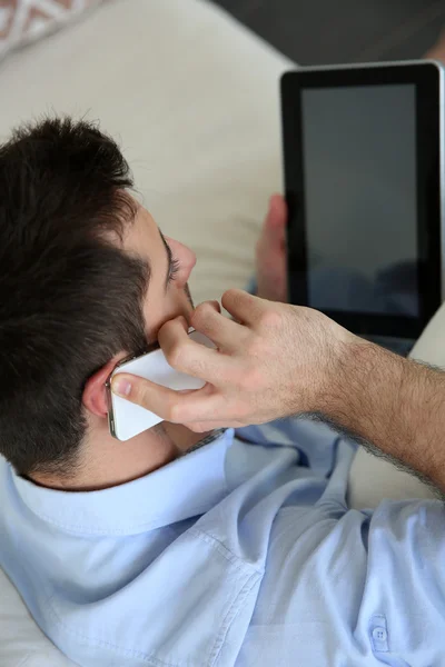 Man sitting in sofa using smartphone and tablet — Stock Photo, Image