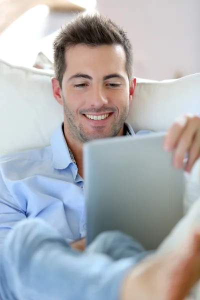 Jovem alegre deitado no sofá com tablet digital — Fotografia de Stock