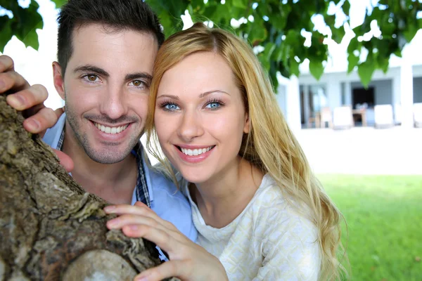 Alegre joven pareja de pie bajo el árbol —  Fotos de Stock