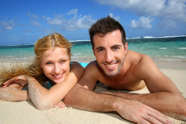 Cheerful young couple laying on a sandy beach — Stock Photo, Image